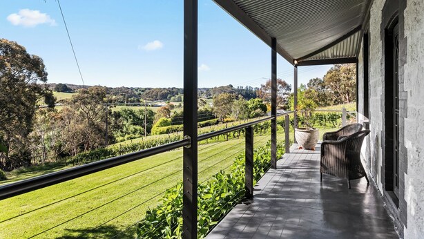 A covered outdoor area with a view of a vineyard, a pergola, and a seating area with wicker furniture. - The Other House (Piccadilly)