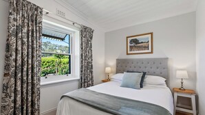 A bedroom with a bed, two bedside tables, a window with curtains, a wall-mounted picture, and a ceiling fan. - The Other House (Piccadilly)