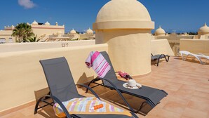 Eine Dachterrasse mit Liegestühlen, Sonnenschirm und Blick auf ein Kuppelgebäude.