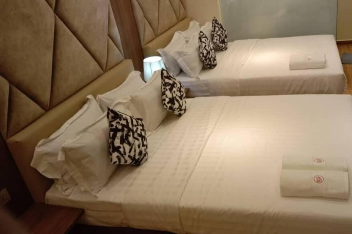 A hotel room with two beds, each with a white bedspread and patterned pillows.