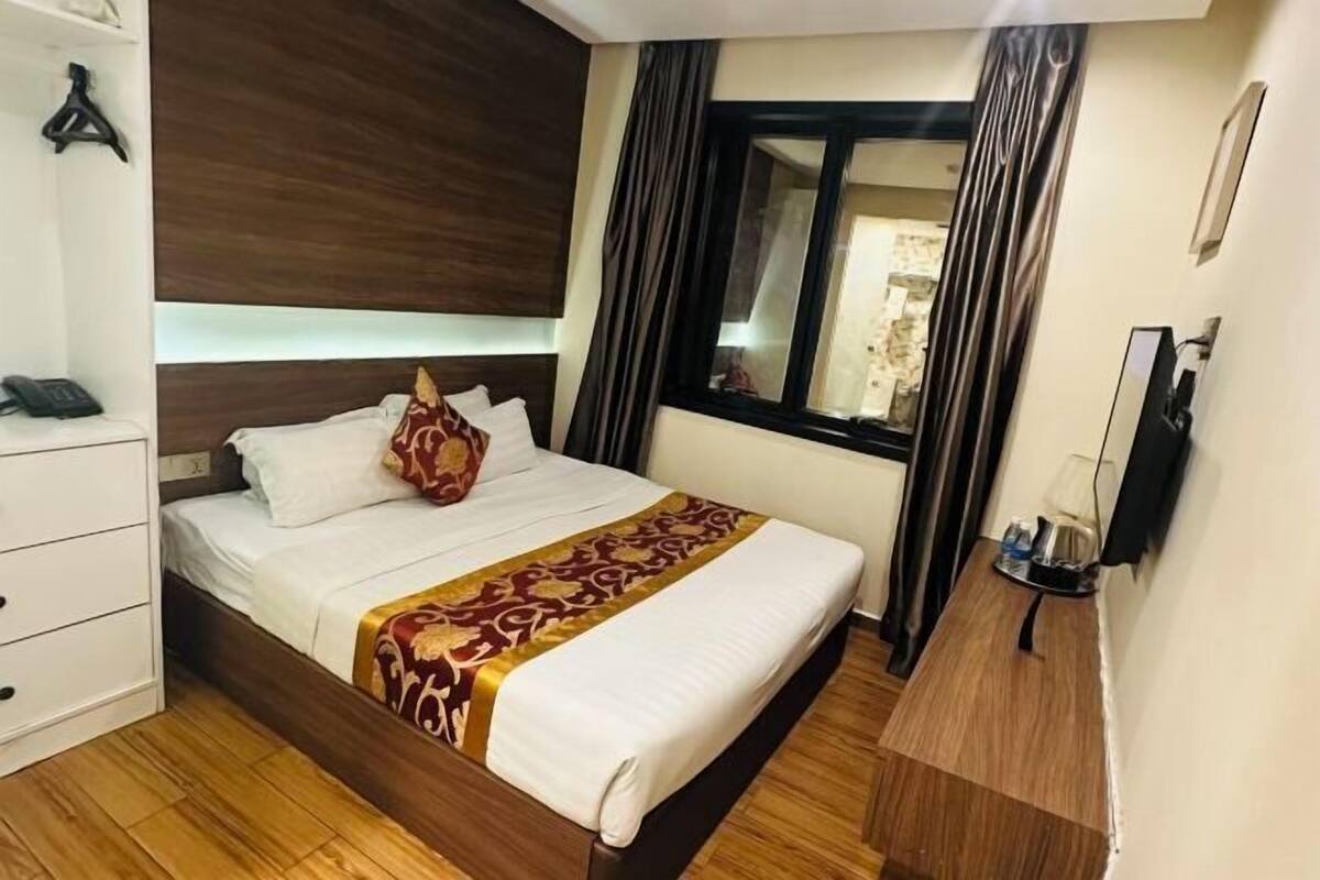 A hotel room with a bed, bedside table, and a window with curtains.