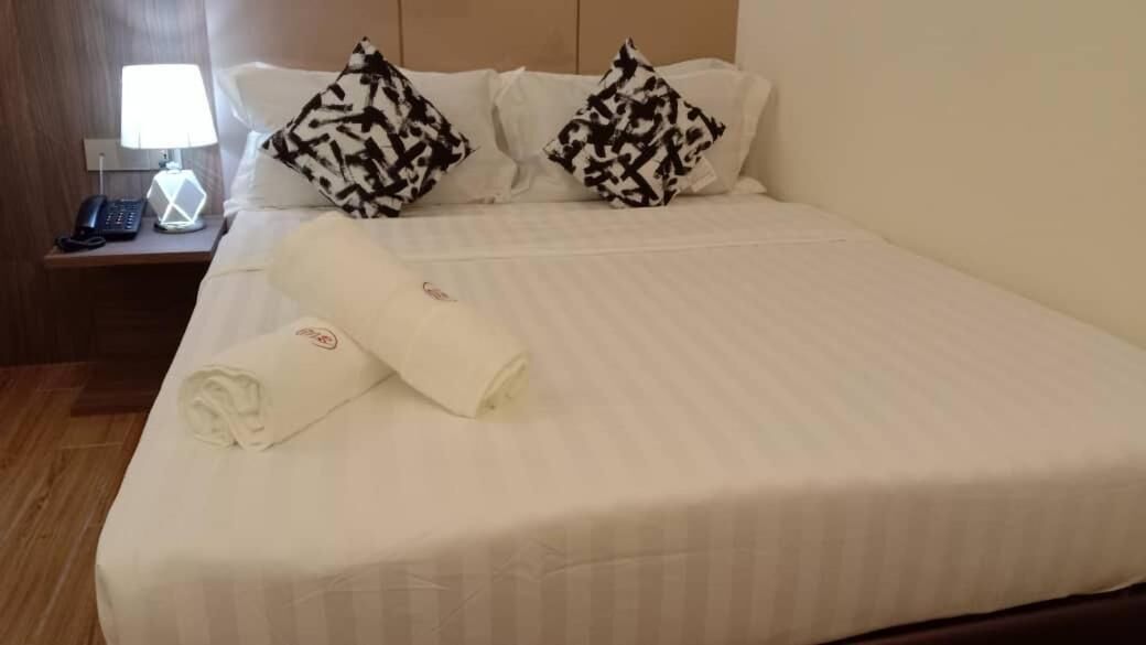 A neatly made bed with white linens, two patterned pillows, and a rolled towel on the side.