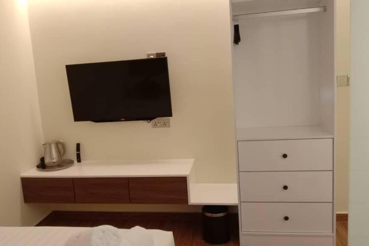 A modern bathroom with a white vanity, a mounted flat-screen TV, a shower area, and a trash bin.