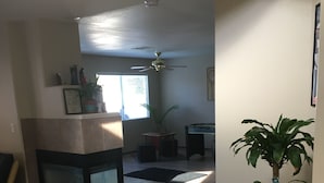 Una sala de estar con chimenea, ventilador de techo y un ventanal grande.