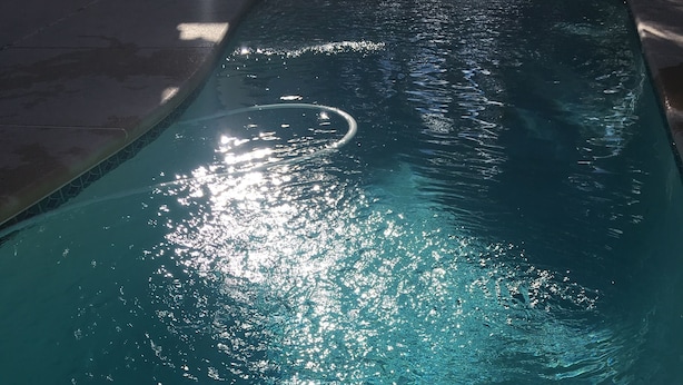 Una piscina con agua cristalina, un desagüe visible y un borde de piscina con textura.