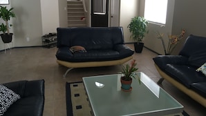 Una sala de estar con un sofá de cuero negro, una mesa de centro de vidrio y una planta en maceta.