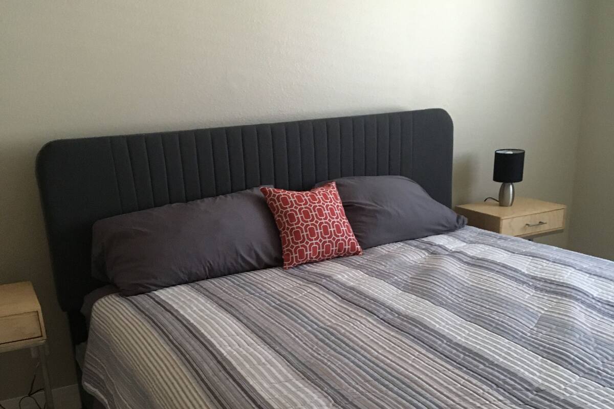 A neatly made bed with striped bedding, a dark headboard, and a small bedside table with a lamp.