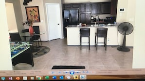 Una habitación con una mesa de comedor, sillas, una cocina con armarios y electrodomésticos, y un ventilador.