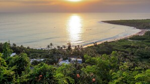 A coastal view with a sunset over the ocean, a beach, and lush greenery. - SkyeBay Club (Hengchun)