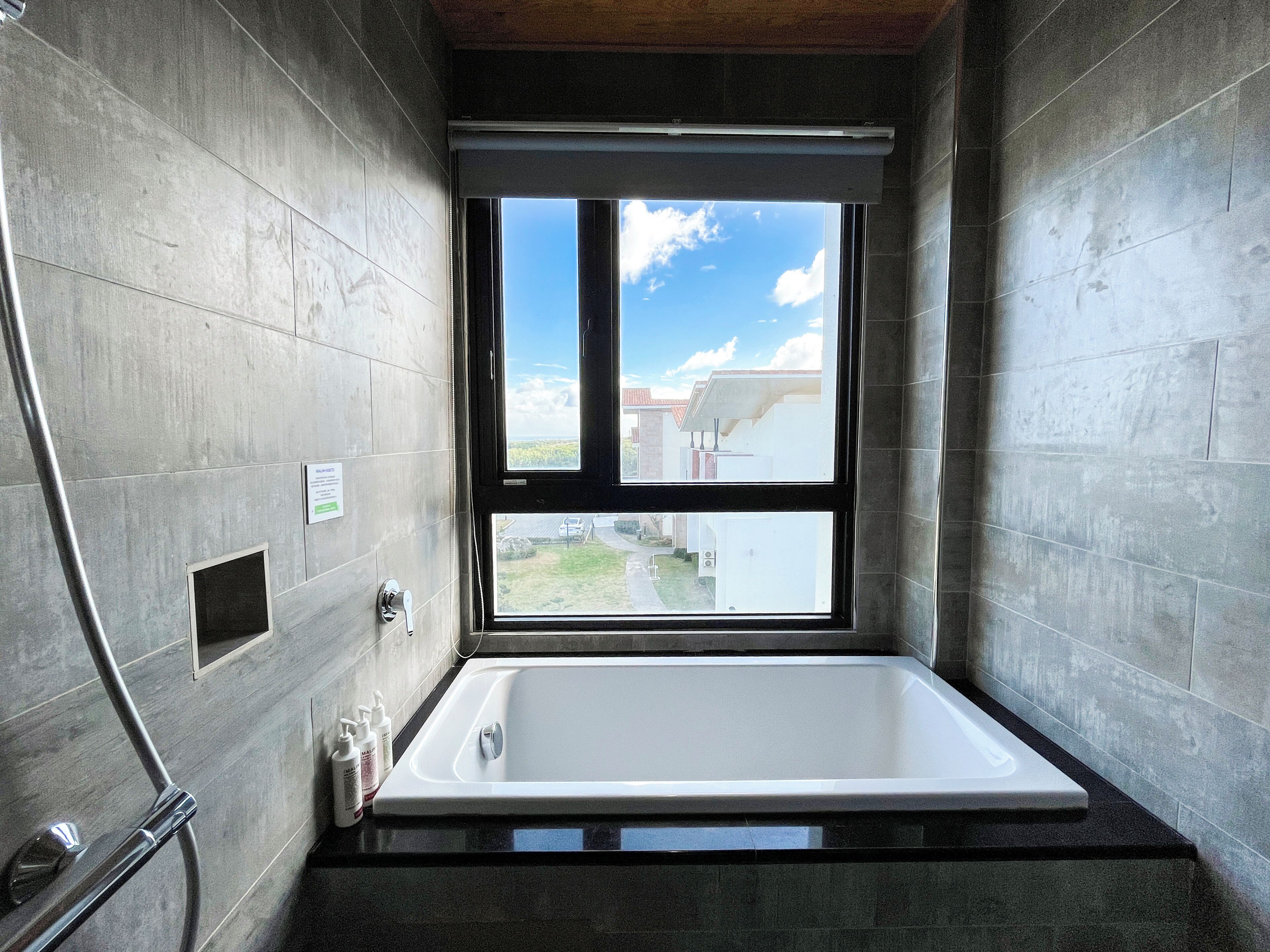 A modern bathroom with a large bathtub, a window with a view of the outside, and a shower area.