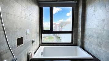 A modern bathroom with a large bathtub, a window with a view of the outside, and a shower area.