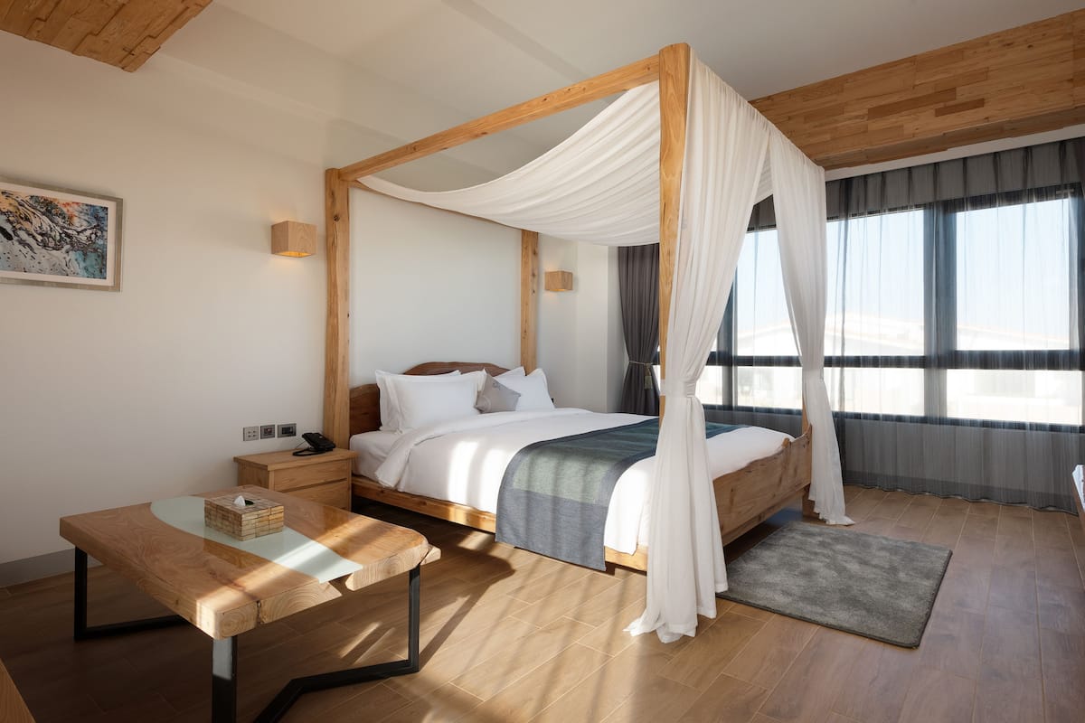 Ein Himmelbett mit weißen Vorhängen, ein Nachttisch mit Taschentuchbox und ein Holznachttisch.