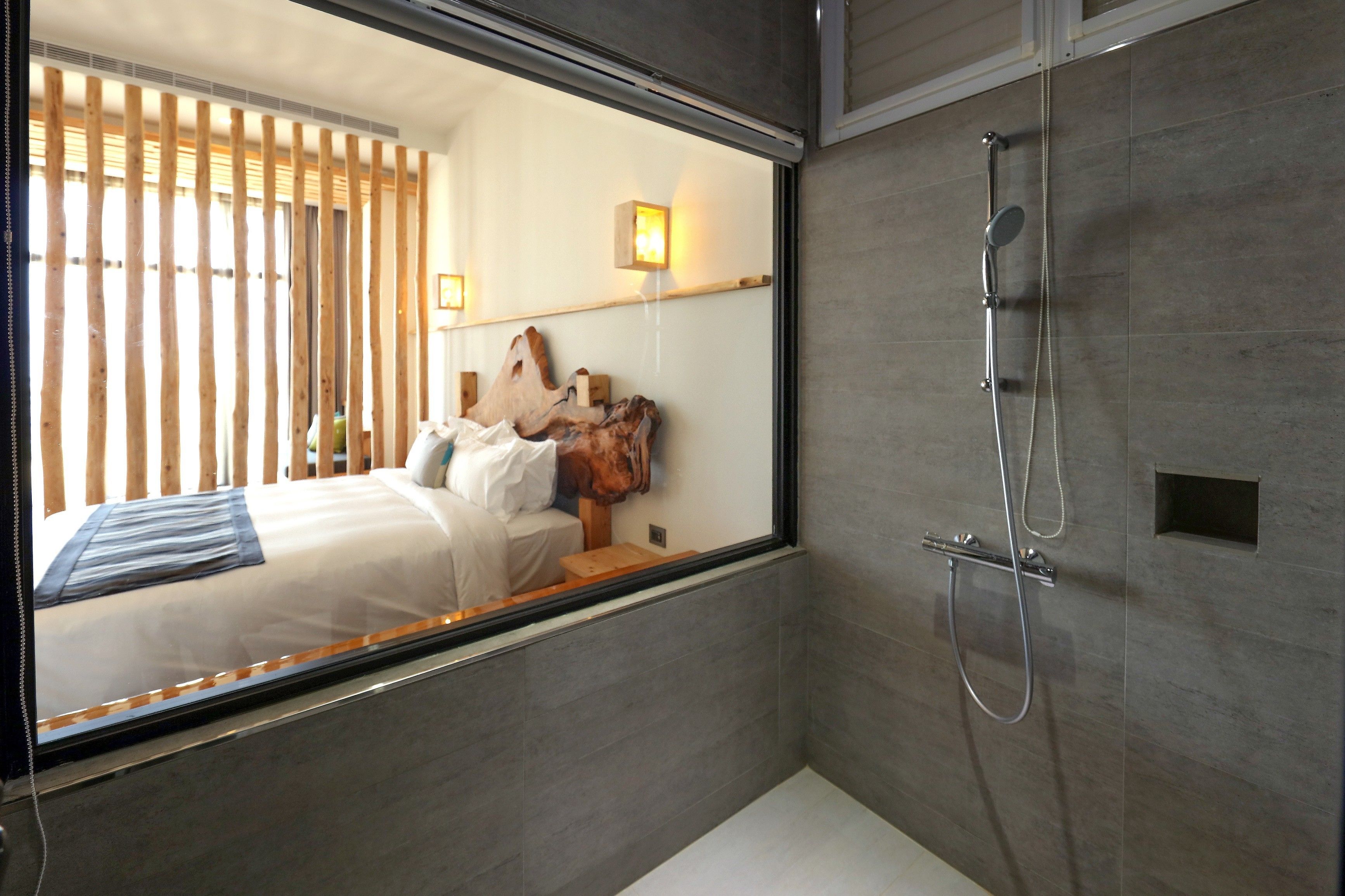 Une salle de bain moderne avec une douche, un lit doté d’une tête de lit en bois et un grand miroir qui reflète la pièce.