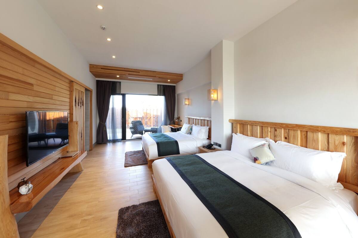 Ein Hotelzimmer mit zwei Betten, einem Fernseher, Holzvertäfelung, einem Balkon und Blick auf die Stadt.