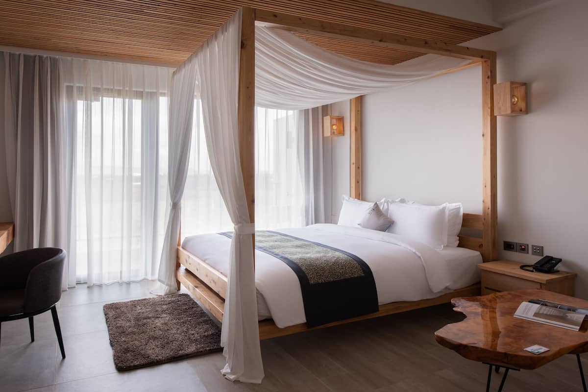 Ein modernes Hotelzimmer mit einem großen Bett, einem Schreibtisch mit Stuhl, einem Holztisch und einem Fernseher.