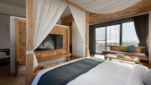 A bedroom with a large bed, a TV mounted on a wooden panel wall, a sofa with cushions, and a view of the outdoors through large windows. - SkyeBay Club (Hengchun)