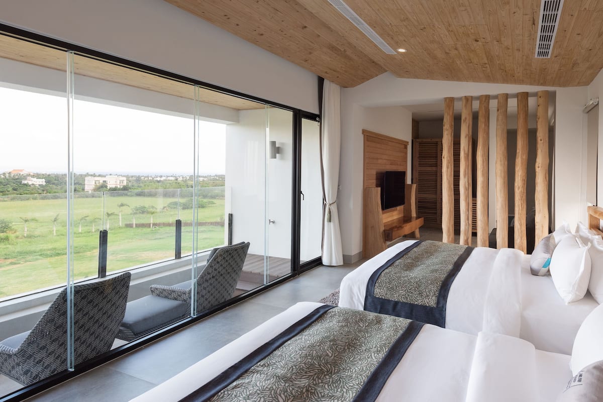 Ein Schlafzimmer mit großem Fenster, einem Bett mit gemusterten Bettbezügen und einem hölzernen Kopfteil.