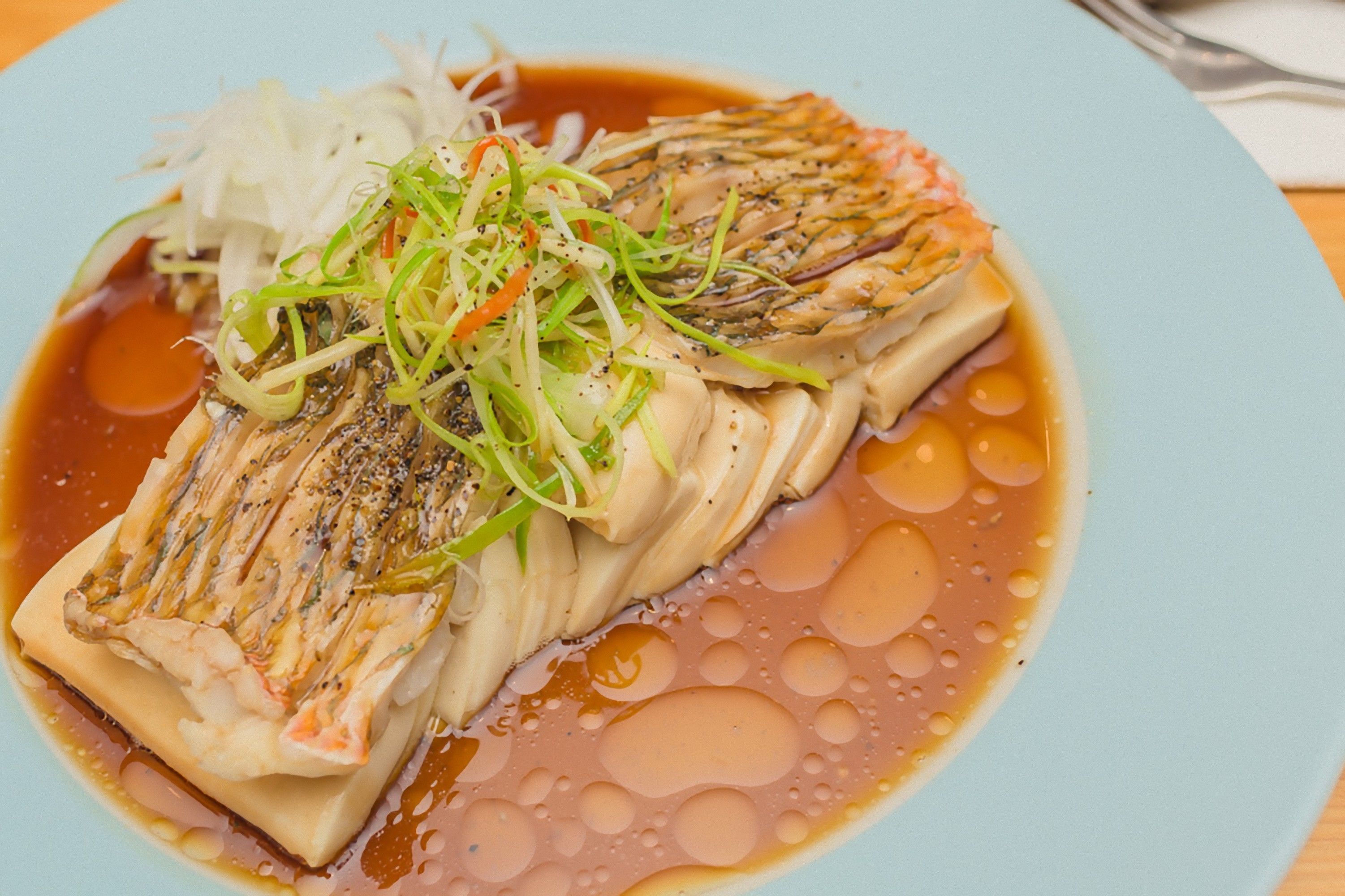 Une assiette de poisson accompagnée d’une sauce légère et de quelques garnitures.