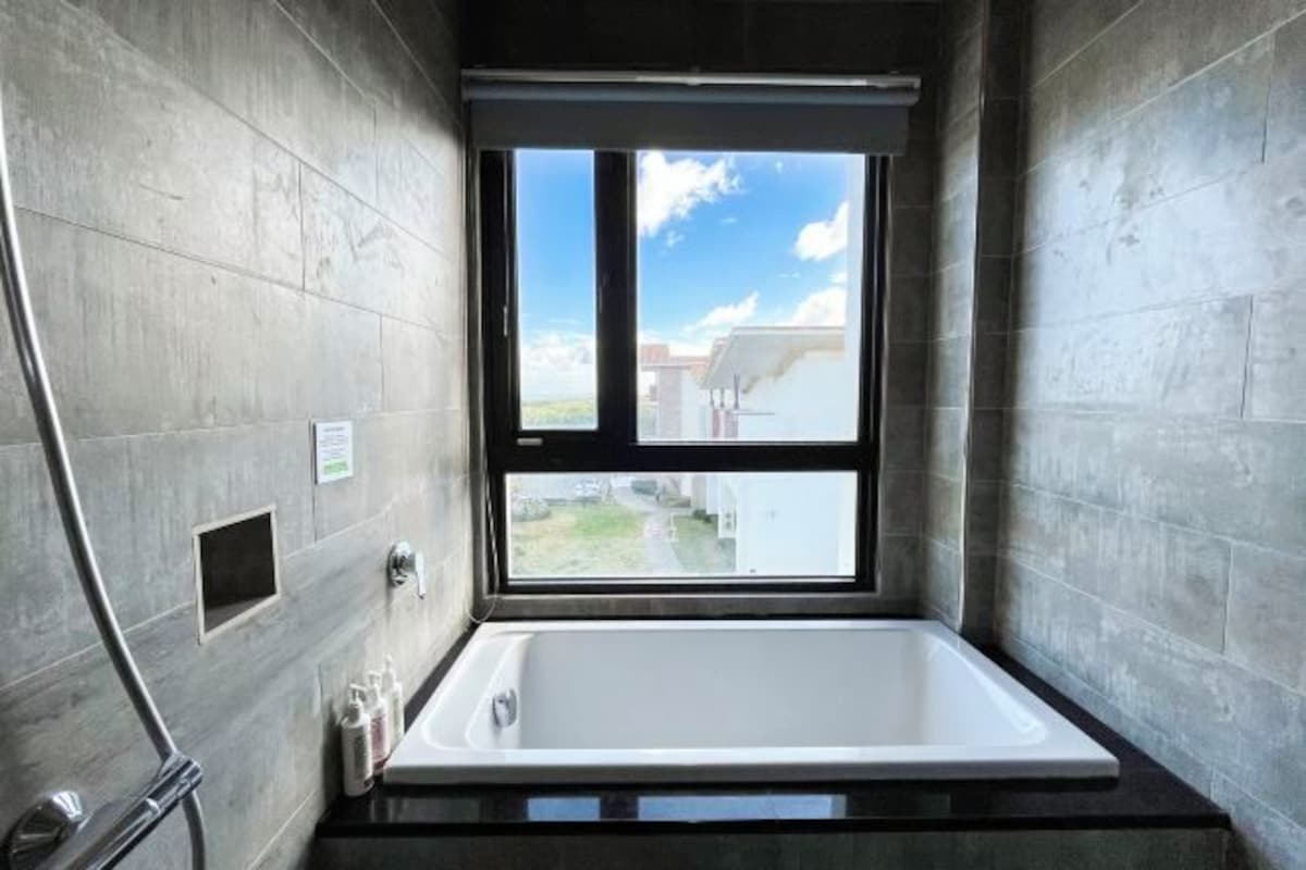 Un baño moderno con bañera, ducha y un amplio ventanal con vistas al exterior.