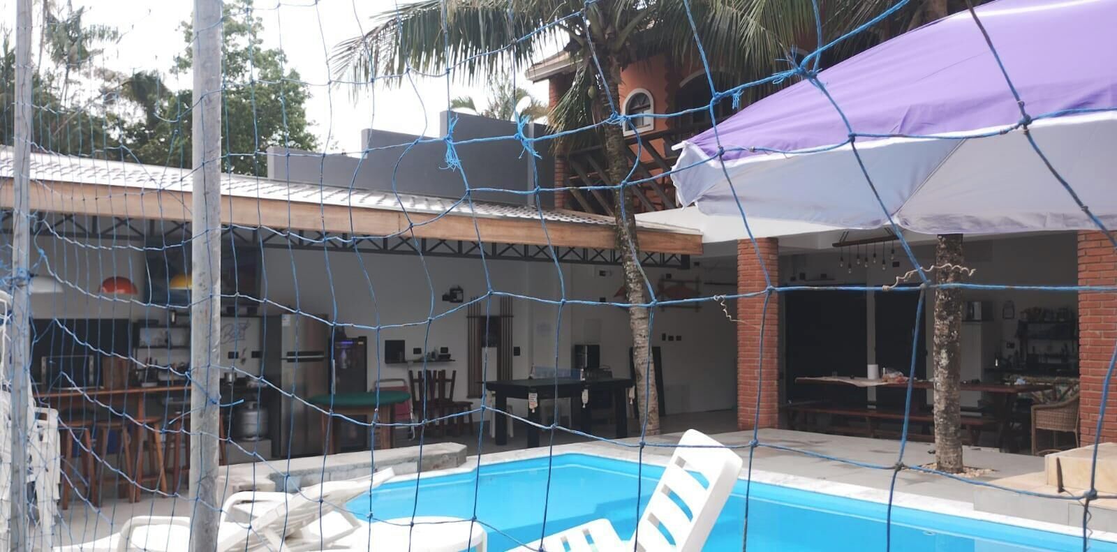 Zona de piscina amb una tanca de xarxa, un pati amb mobles d'exterior i un edifici amb façana de maó.