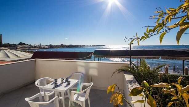 A terrace with a table and chairs, overlooking a coastal view with a clear sky and sun. - A seafront, one bedroom apartment with big terrace - Umag Center 1 (Umag)