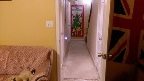 Un couloir étroit, avec un canapé à motifs sur la gauche et une porte ornée d’un motif Union Jack sur la droite. Une affiche sur le thème de Noël est accrochée au mur.