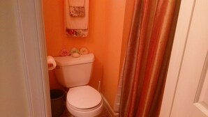 Une petite salle de bain avec un mur orange, des toilettes, une poubelle et un rideau de douche.