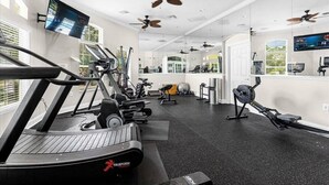 Ein modernes Fitnessstudio mit verschiedenen Trainingsgeräten, großen Fenstern und Deckenventilatoren.