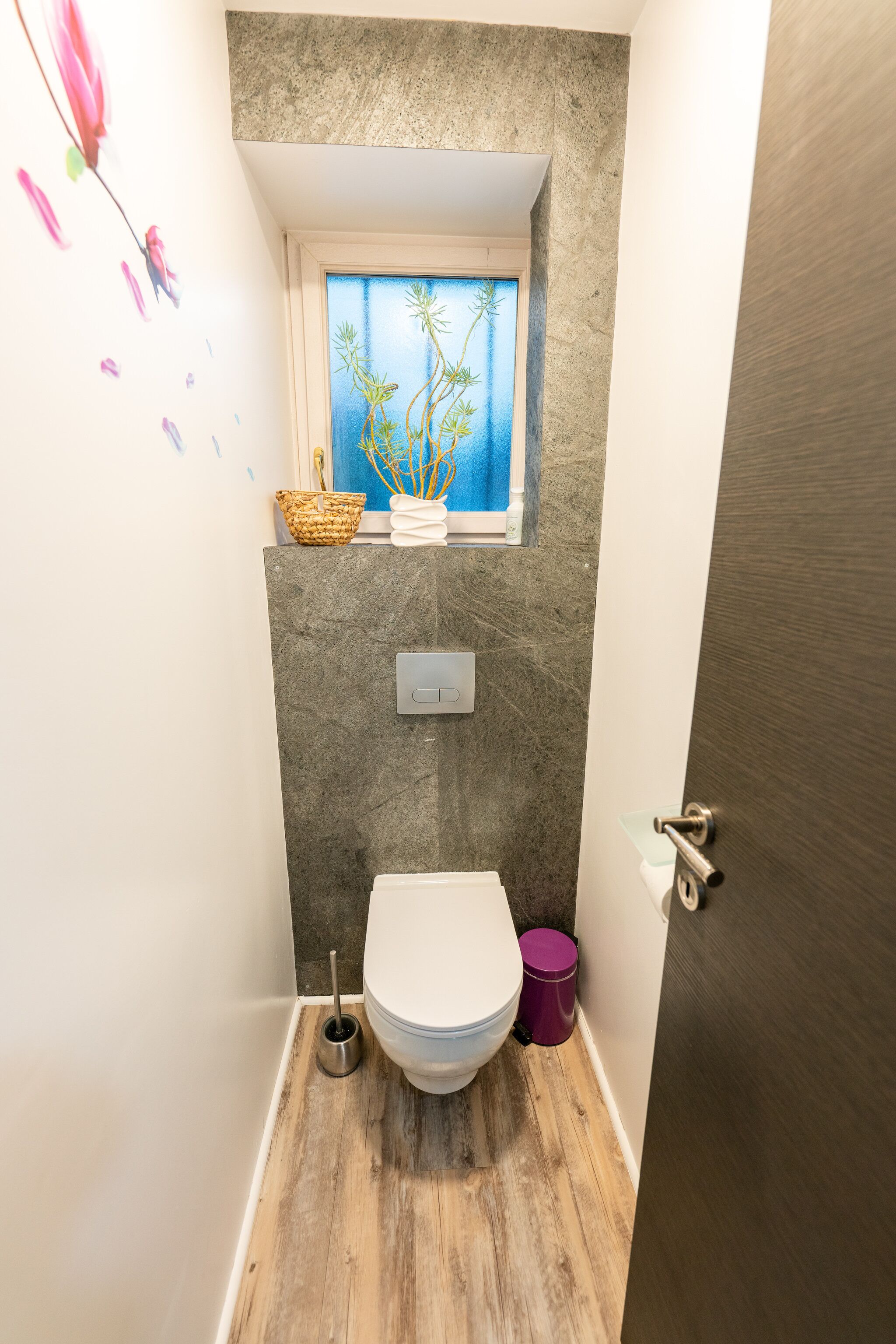 Un baño pequeño con inodoro, ventana con vistas, estante y cubo de basura.