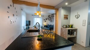 Eine moderne Küche mit schwarzem Arbeitsplatz, einer Schale mit Pflanzen und einem 'HOME'-Schild. Es gibt eine Holzbalkendecke und eine hängende Leuchte.
