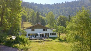Una casa bianca con veranda, circondata da alberi e una collina sullo sfondo.