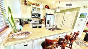 A kitchen with a large island, white cabinets, stainless steel appliances, and wooden chairs.