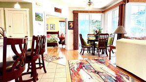 A spacious room with a large bed, a dining area with chairs and a table, and a view through the windows.