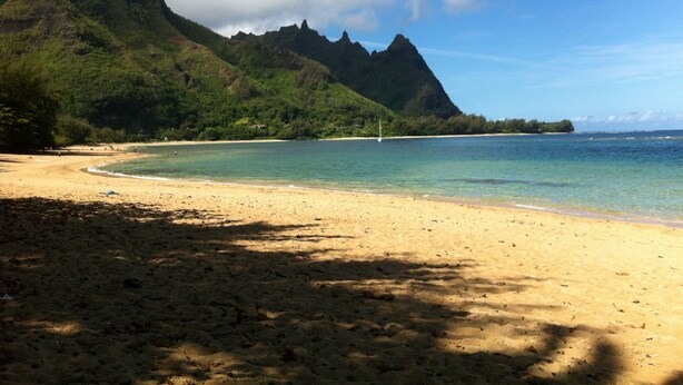 A beach with clear turquoise water, a sandy shore, and a mountain in the background.