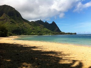 Ein Strand mit klarem Wasser, einer Segelyacht und einem Berg im Hintergrund.