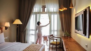 A hotel room with a bed, a desk, a chair, a TV, and curtains. - Ndalem Nuriyyat Villas & Spa (Ngaglik)