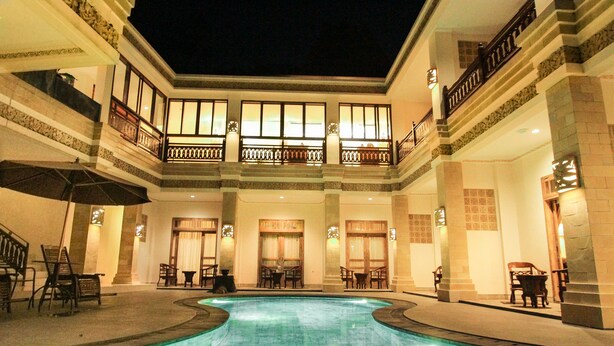 A large indoor swimming pool with multiple levels of balconies and seating areas. - Ndalem Nuriyyat Villas & Spa (Ngaglik)