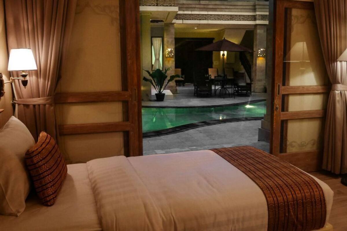 A hotel room with a bed, a nightstand, a lamp, and a view of an outdoor pool area.