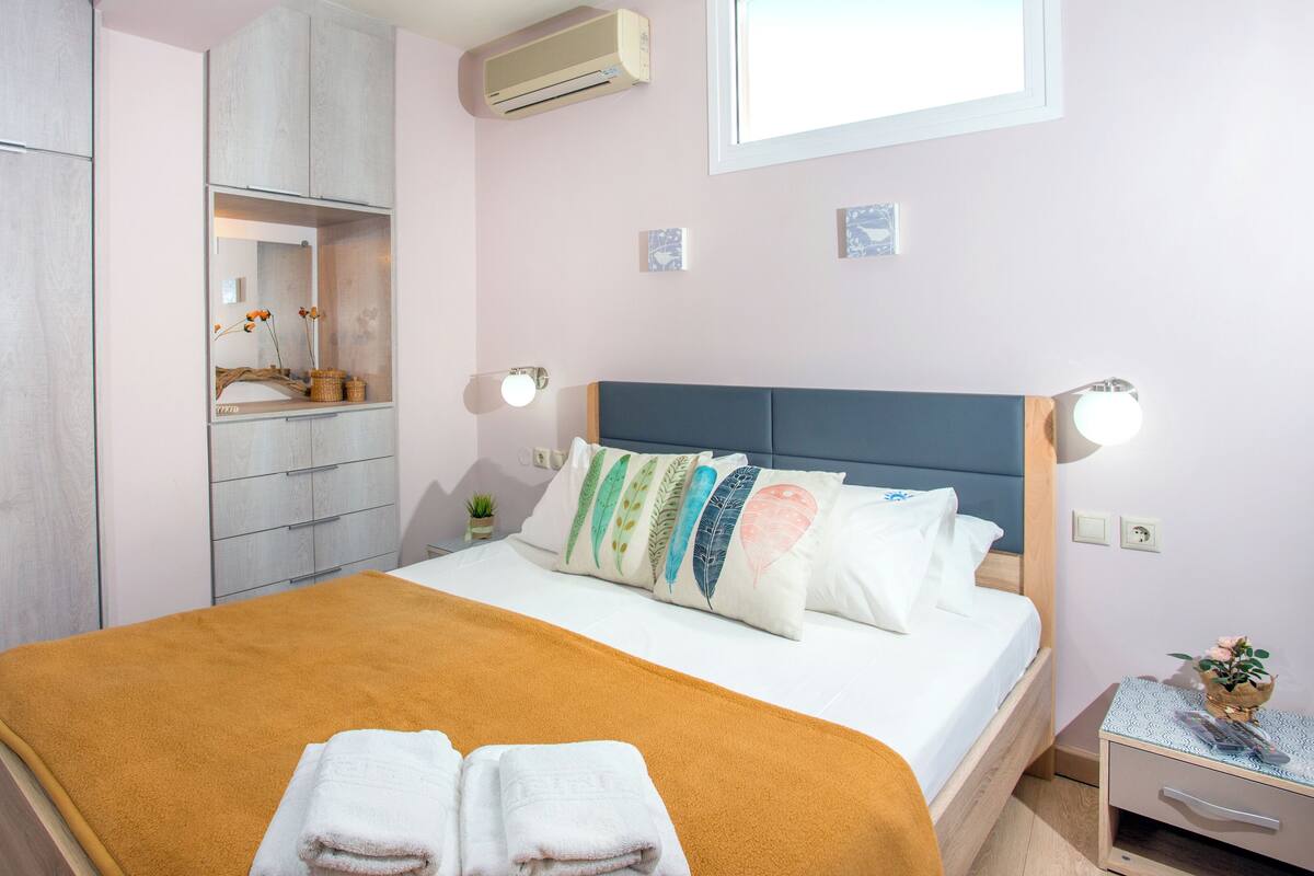 A bedroom with a bed, a wardrobe, a mirror, a nightstand, and a window.