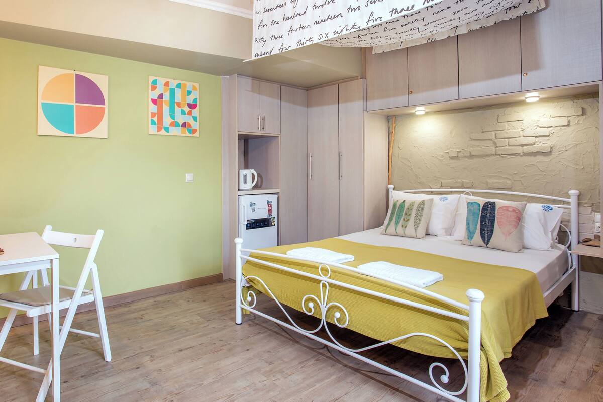 A room with a bed, a desk, and a chair. There are three artworks on the wall.