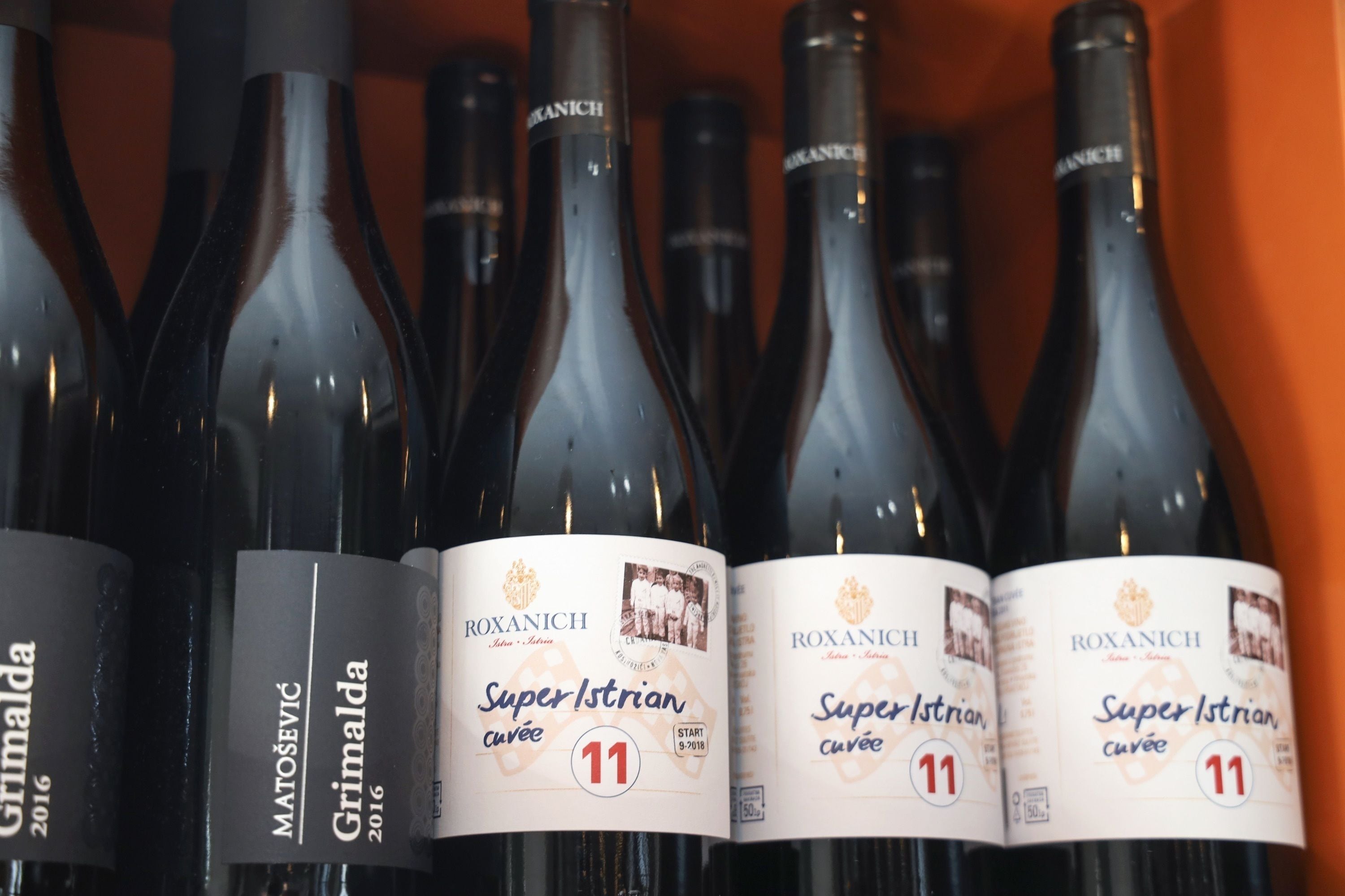 A row of wine bottles with labels indicating 'Roxanich Super Istrian cuvée' and 'Grimalda 2016'.