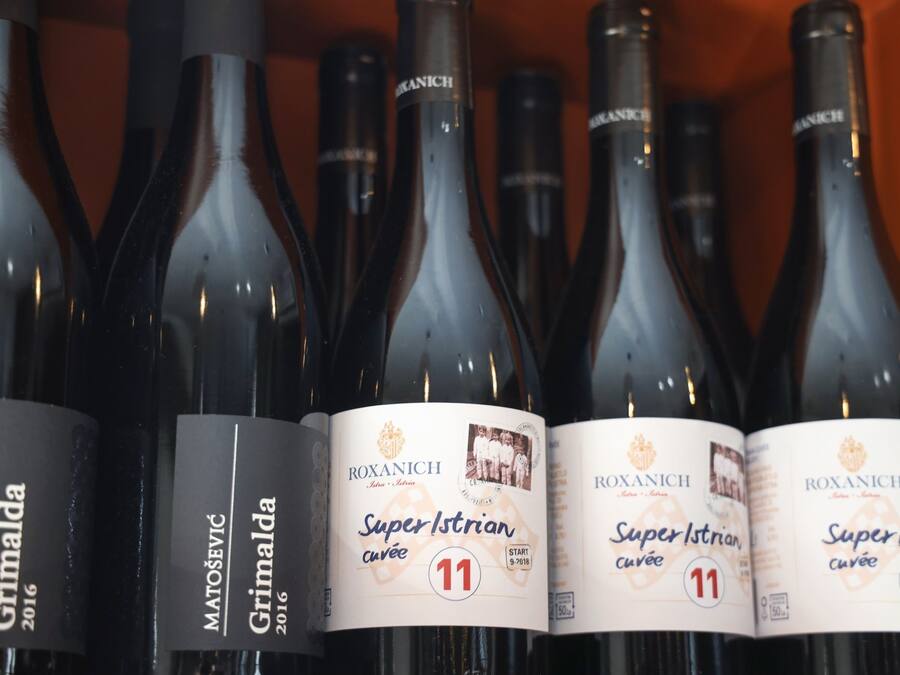Una hilera de botellas de vino con etiquetas que indican 'Roxanich Super Istrian cuvée' y 'Grimalda 2016'.
