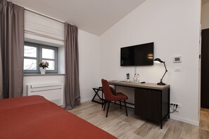 Een moderne slaapkamer met een bed, een bureau, een stoel, een televisie en een raam met gordijnen.