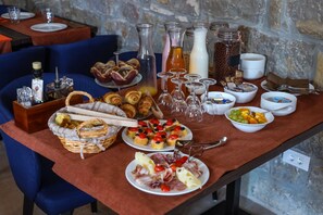 Een ontbijtbuffet met diverse gerechten, waaronder gebak, fruit en drankjes, gepresenteerd op een tafel met een achtergrond van een stenen muur.