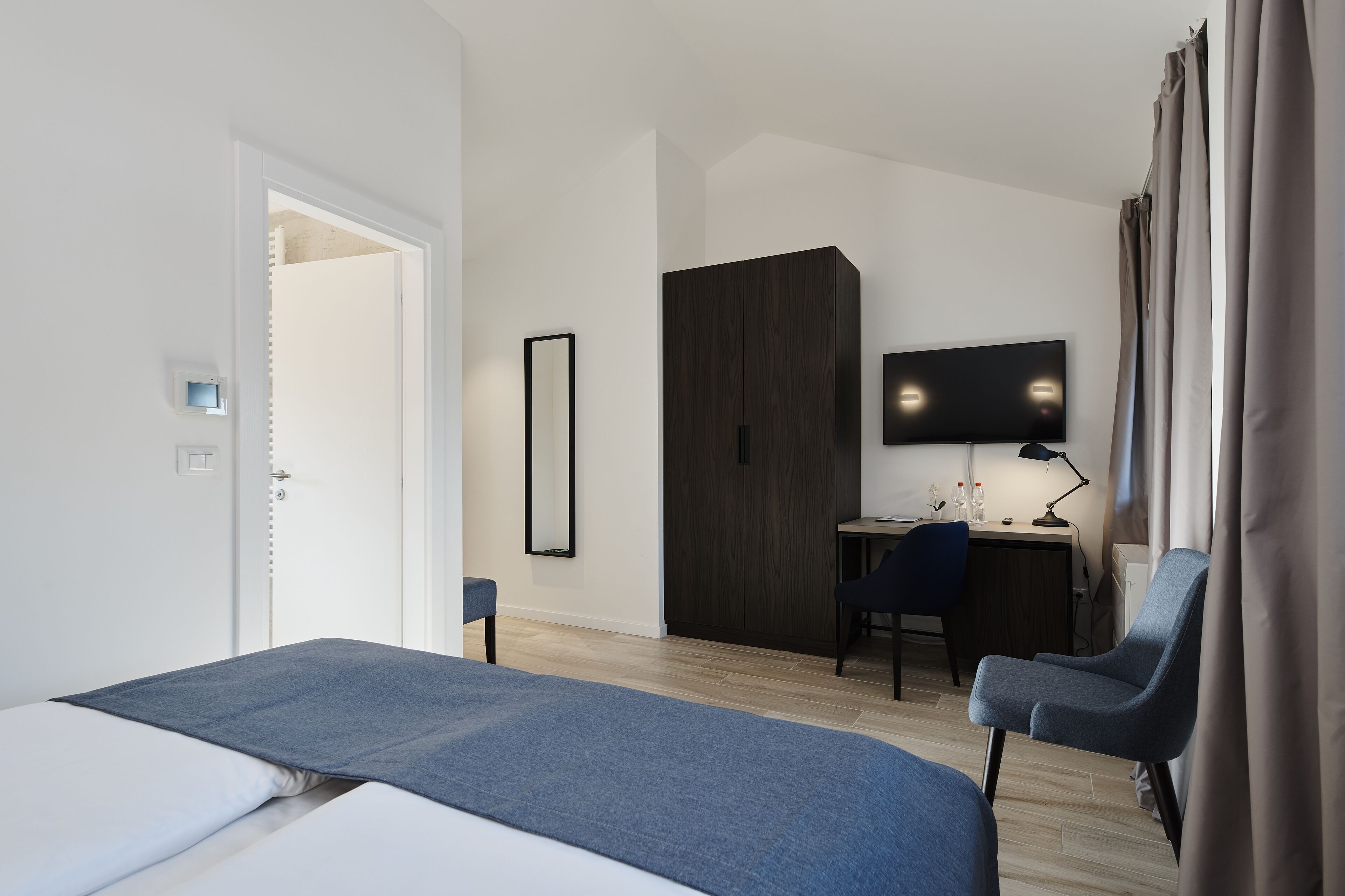 A hotel room with a bed, a desk, a chair, a television, and a wardrobe.