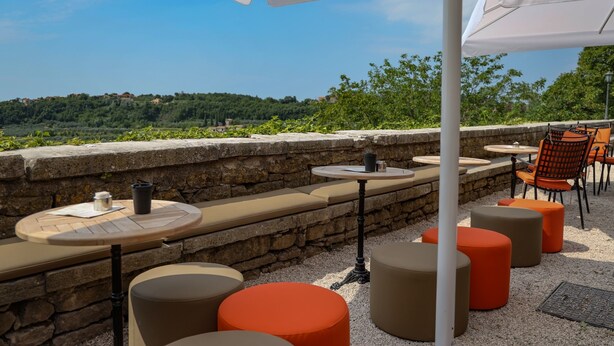 An outdoor seating area with round tables and orange stools, stone walls, and a view of a green landscape. - B&B Artegnana 1798 (Groznjan)