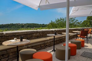 An outdoor seating area with round tables and orange stools, stone walls, and a view of a green landscape. - B&B Artegnana 1798 (Groznjan)