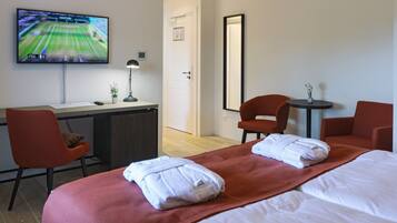 A hotel room with a bed, two red chairs, a desk with a TV, and a small table with a plant.