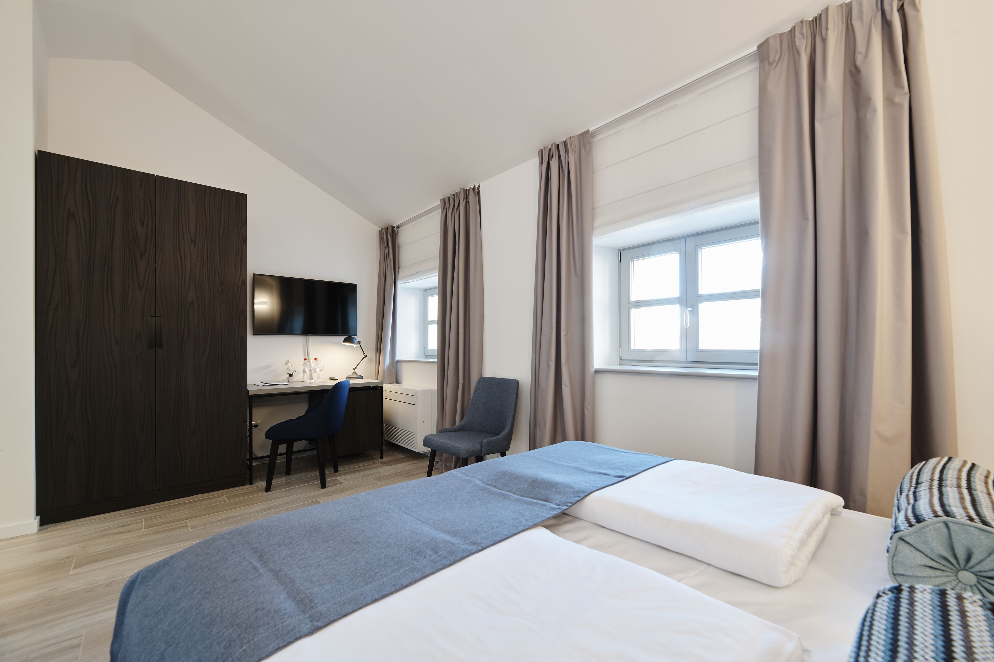 Una habitación de hotel con cama, escritorio, silla, armario y ventana.