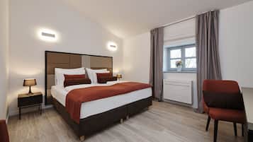 A modern hotel room with a large bed, bedside lamps, a window with curtains, a radiator, and a chair.